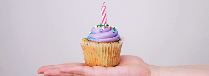 A hand holding a cupcake with a single candle in it