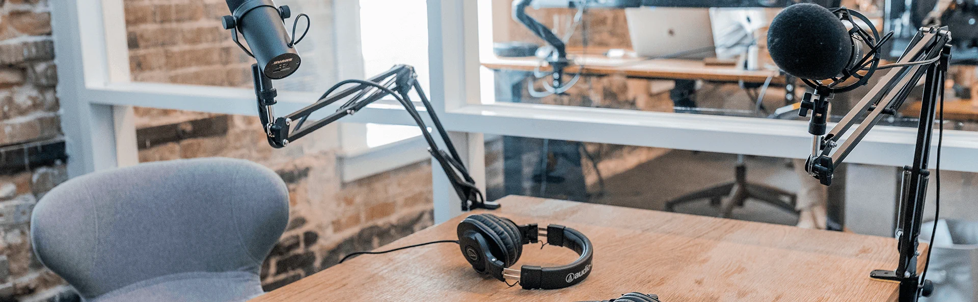 A podcast recording setup with microphones on adjustable arms, headphones, and a mixing console on a wooden table in a studio.