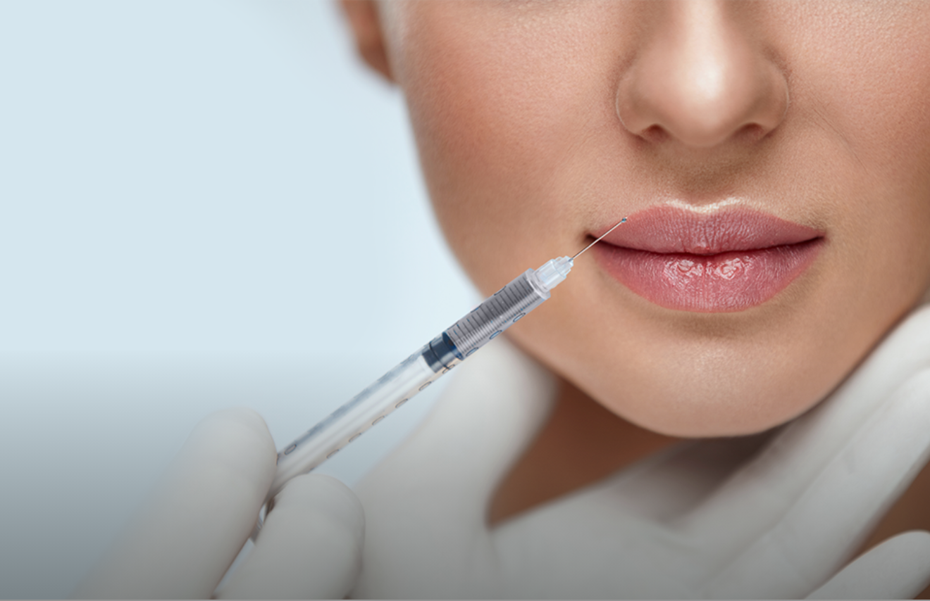 A close-up of a person receiving a lip injection from a syringe held by a gloved hand.