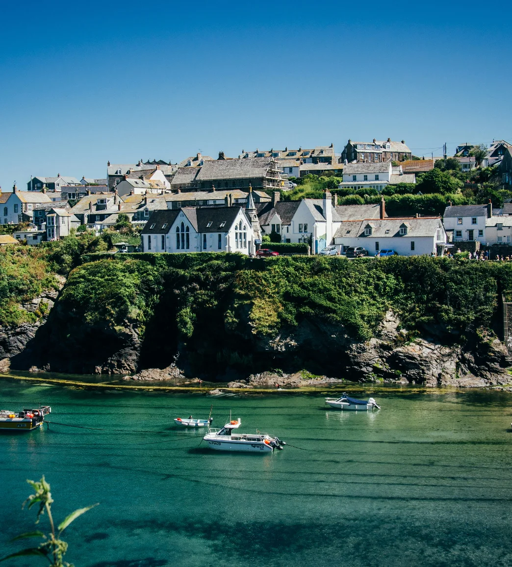 A coastal village with houses on a hillside overlooking a clear blue bay with several small boats anchored.