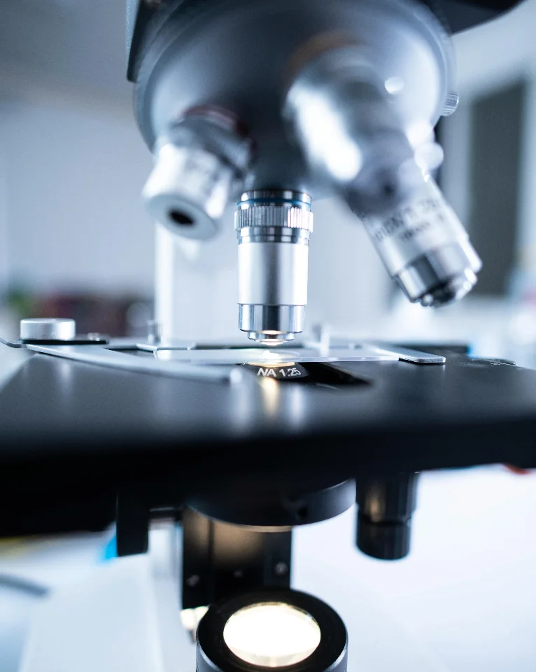 Close-up view of a microscope lens focused on a slide with bright illumination from below.
