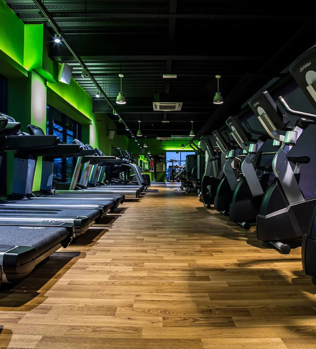 A row of treadmills lines one side of a modern gym with green accent lighting.