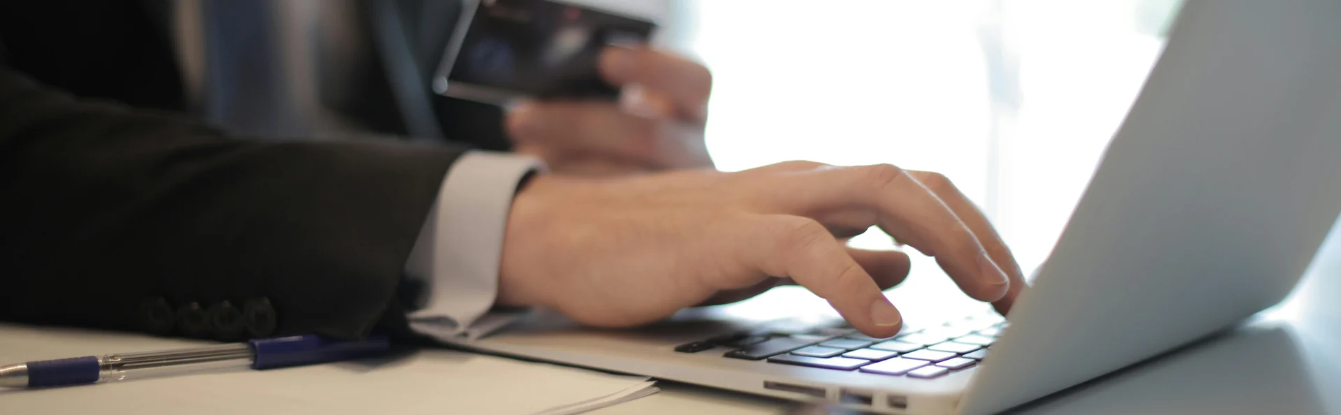 A person in a suit uses a laptop while holding a credit card, likely making an online transaction, possibly integrating Google Consent Mode v2 for enhanced user privacy.